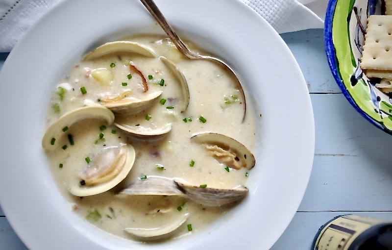 clam chowder in a white bowl with a pale bowl board background